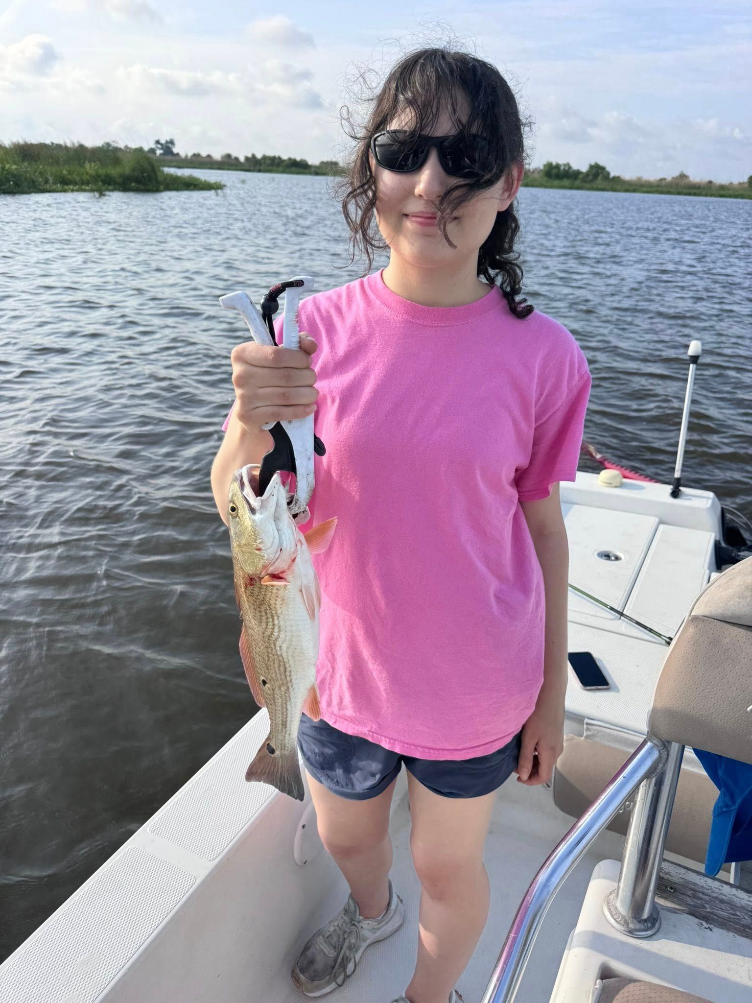 A young girl is standing on a boat holding a fish.