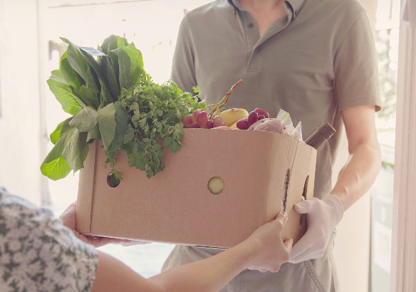 A man is delivering a box of vegetables to a woman.