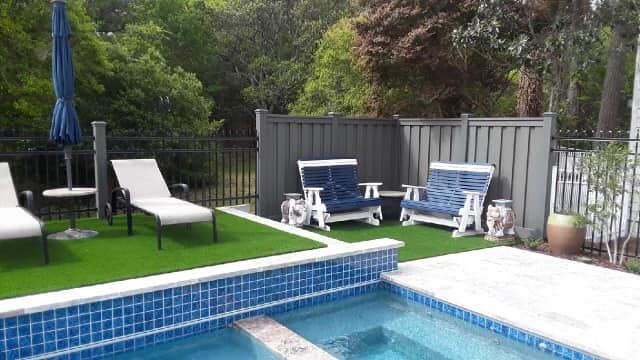 Poolside scene with lounge chairs, umbrella, and a small seating area with two armchairs and a privacy fence.