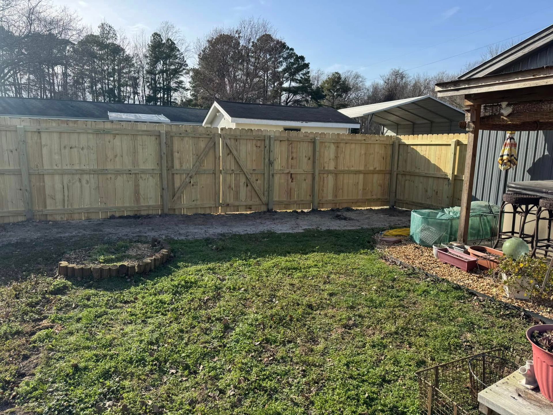 Backyard with wooden fence, gate, and green grass, near a house and trees.