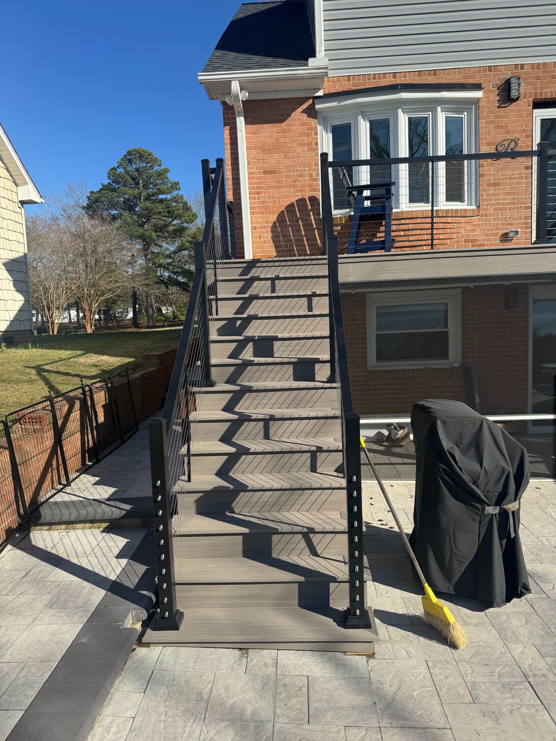 Brick townhouse with a steep outdoor staircase and black railings in a sunny front yard