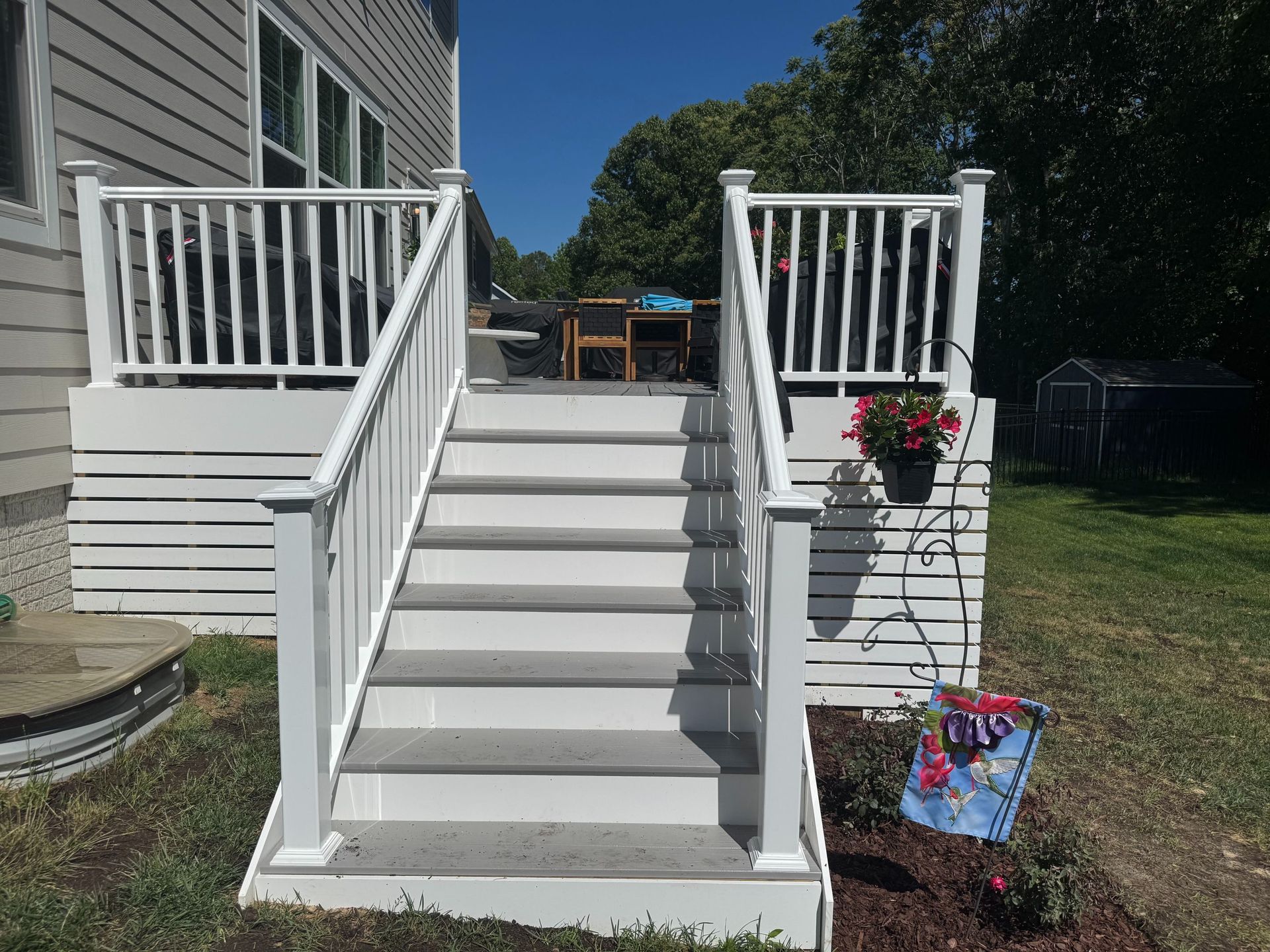 White front steps with railings leading to a porch, with hanging flower baskets and a small garden sign.