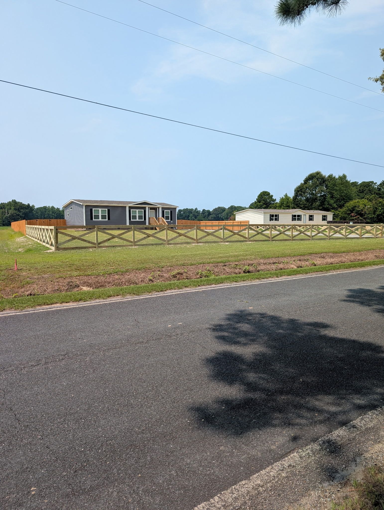 Rural roadside view with a grassy field, two small buildings, and a clear blue sky.