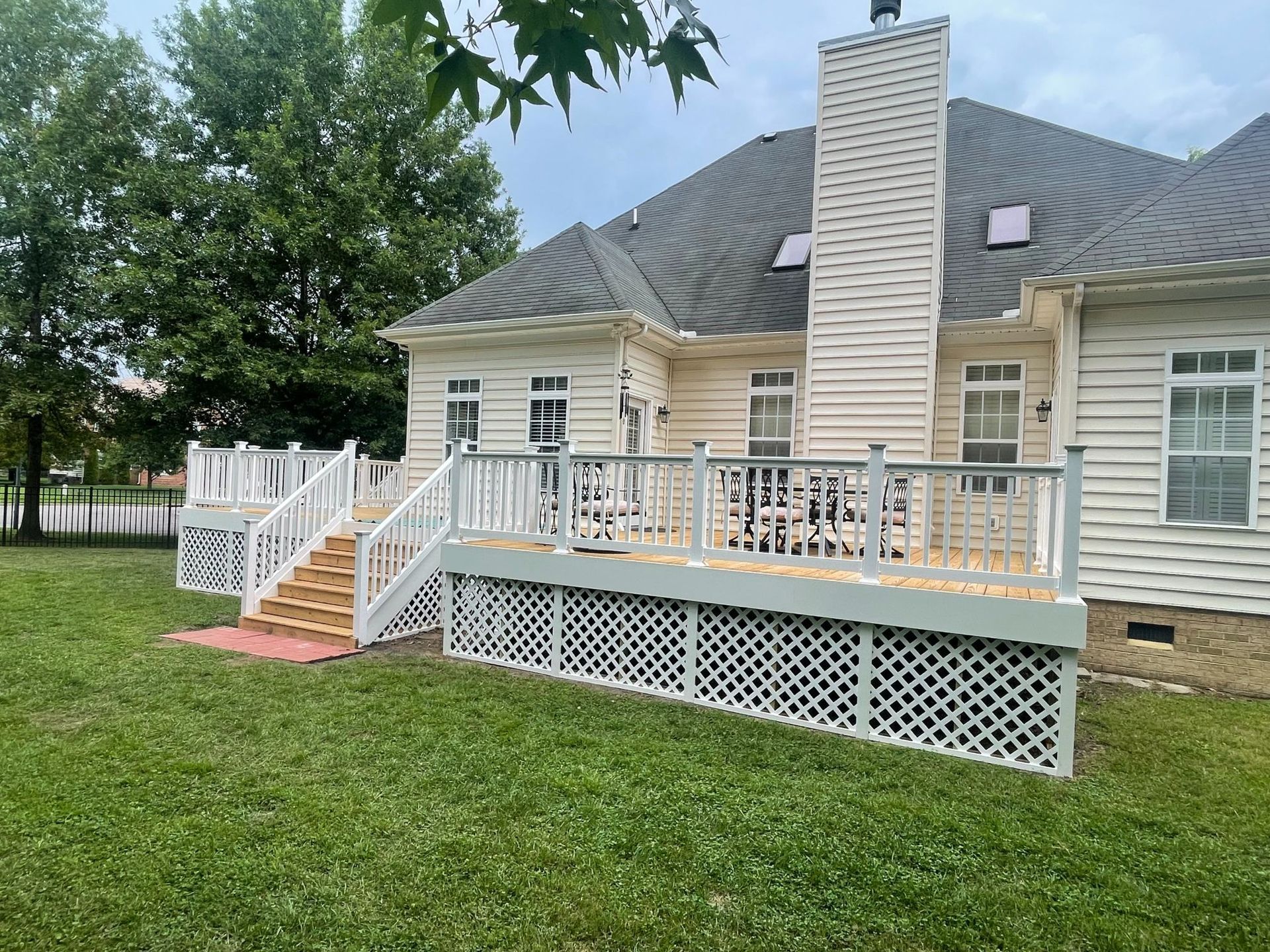 House with raised deck, white railings, and lattice skirting in a grassy yard