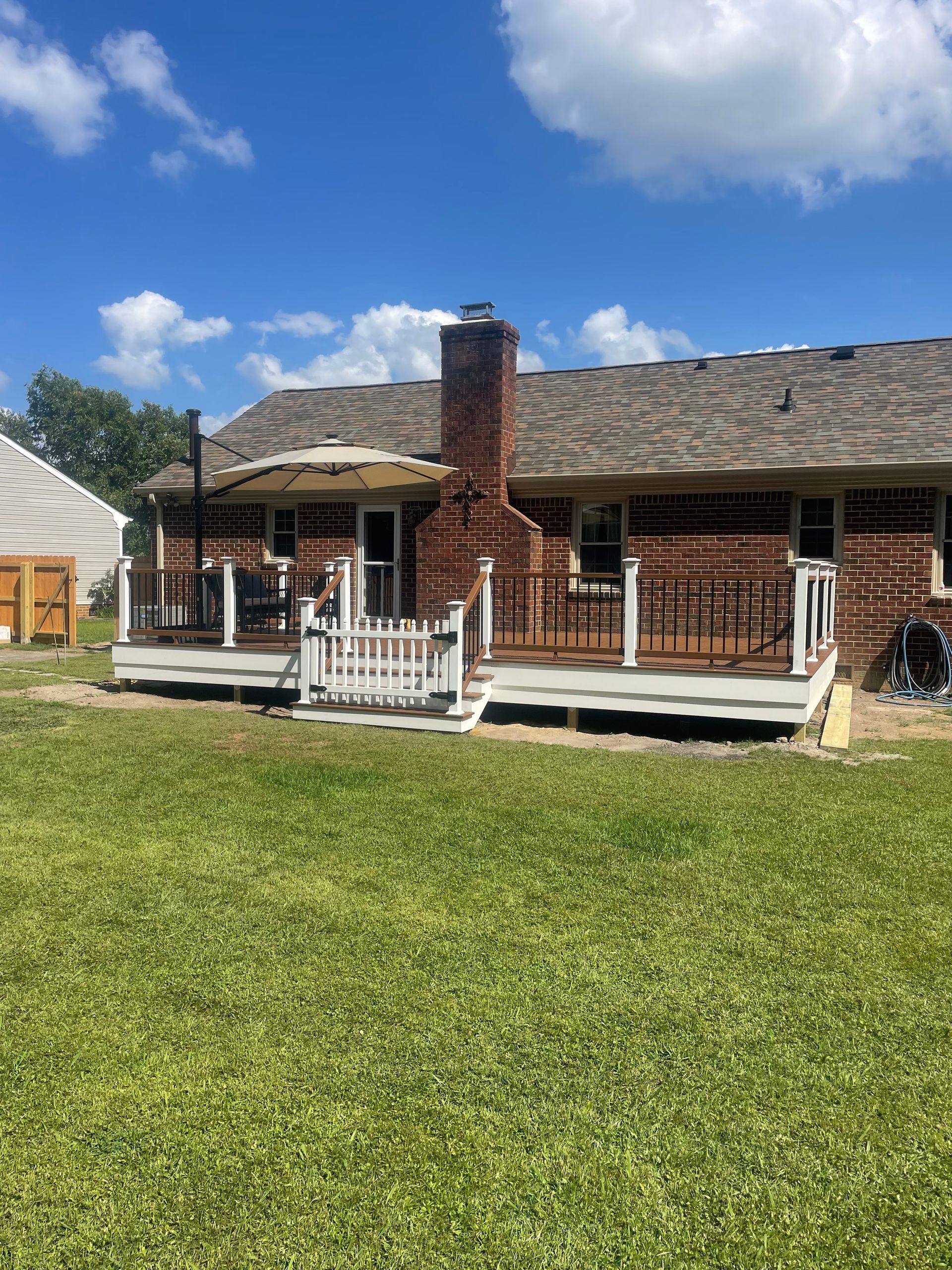 Backyard view of a brick house with a deck, chimney, and green lawn under a blue sky.