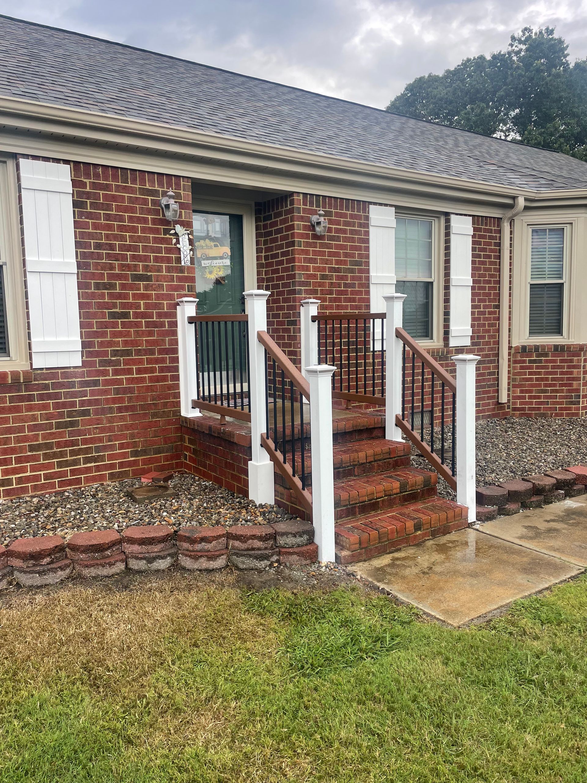 Red brick home with white shutters, steps, and railing leading to the front door on a cloudy day.