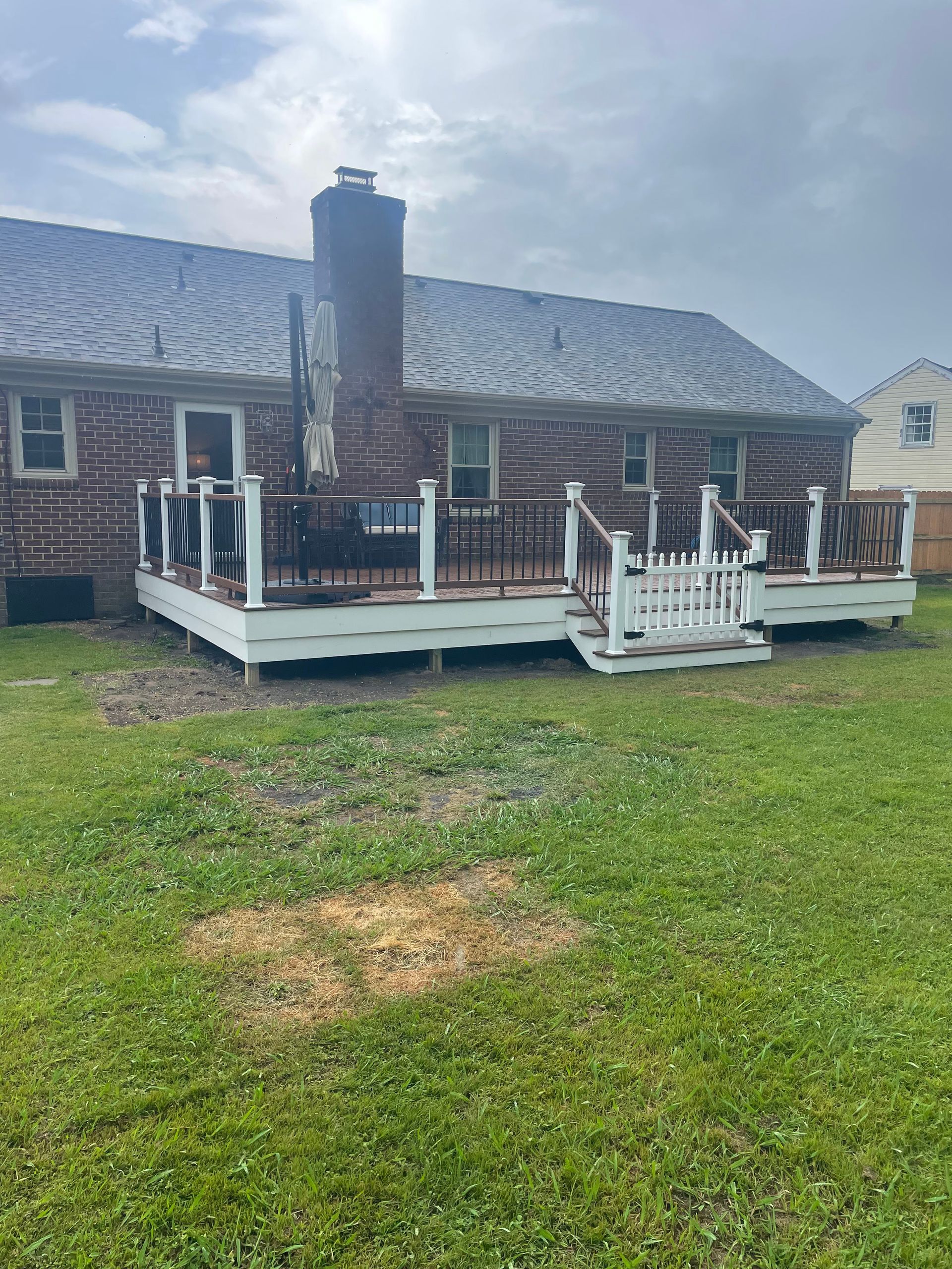 Backyard view of a red brick house with a wooden deck, green grass, and a gray sky.