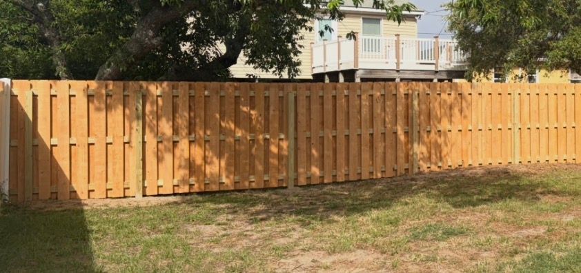 Wooden privacy fence across a grassy yard with trees and a house behind it