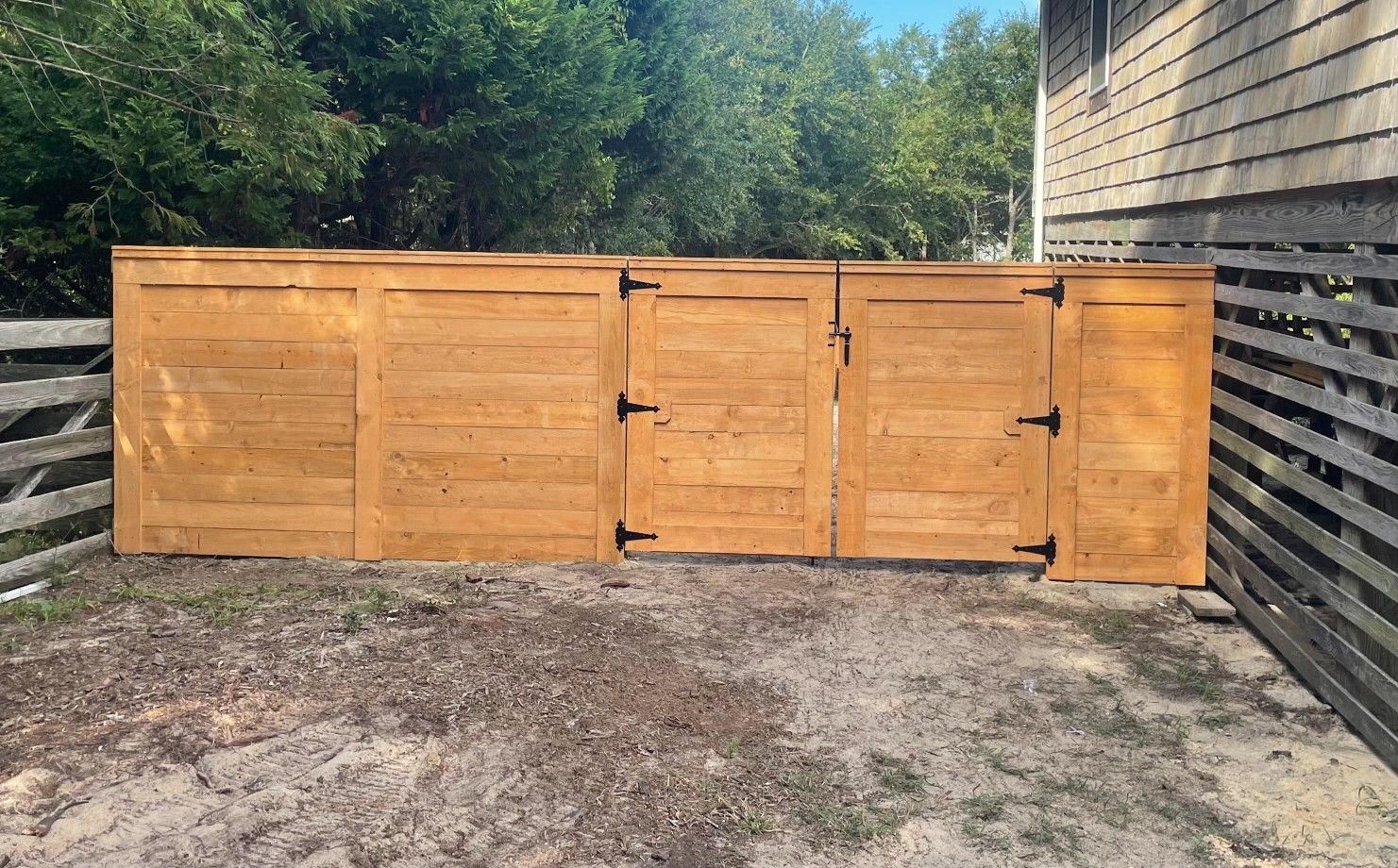 Wooden fence with three sections, including a gate, next to a house.
