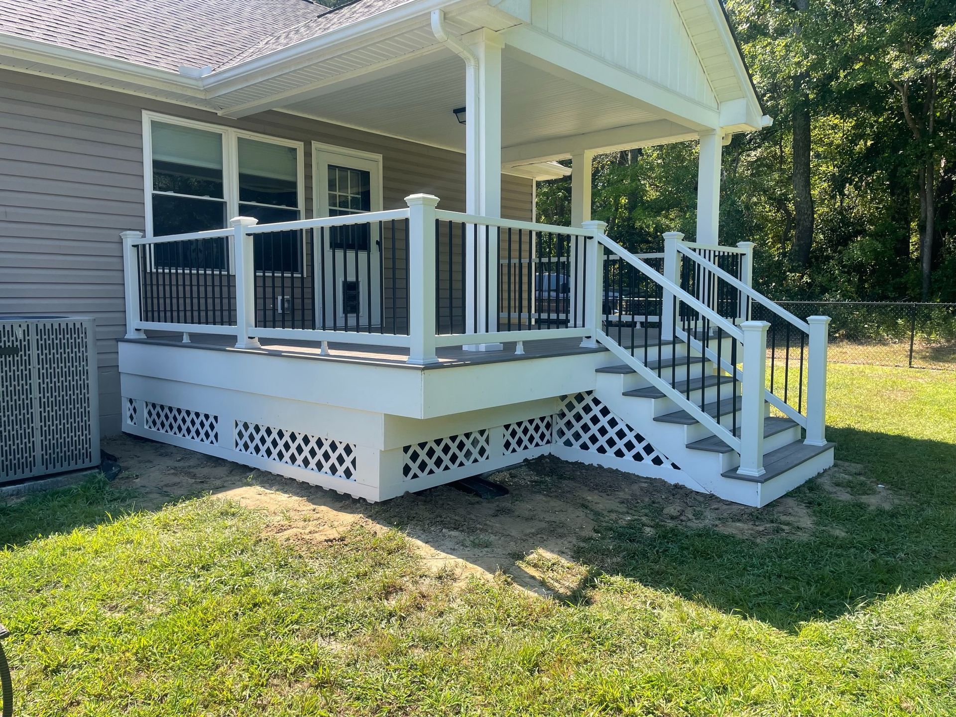 A deck with stairs, white railings, and black spindles, attached to a house, on a grassy lawn.
