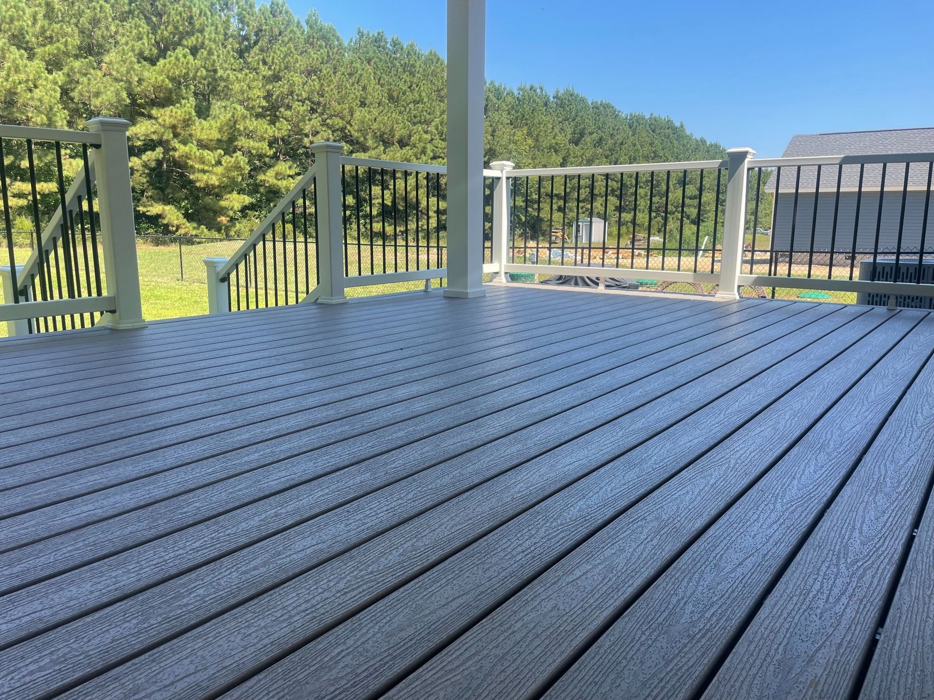 Gray composite deck with white railings and black balusters, overlooking a wooded area.