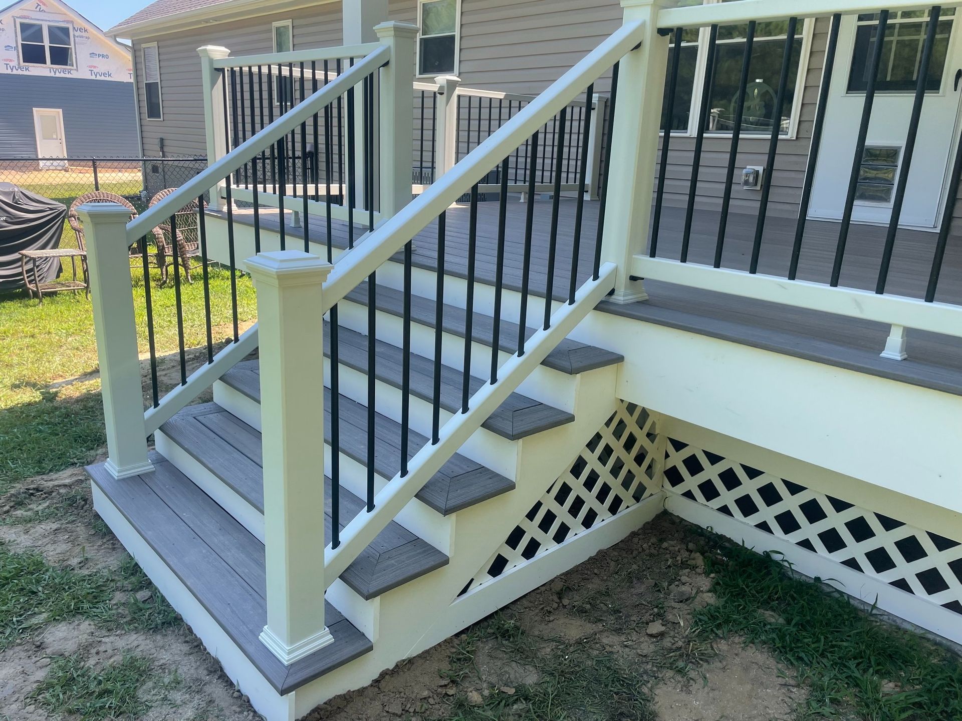 A wooden deck with stairs and black railings. White trim, grey steps, and latticework.