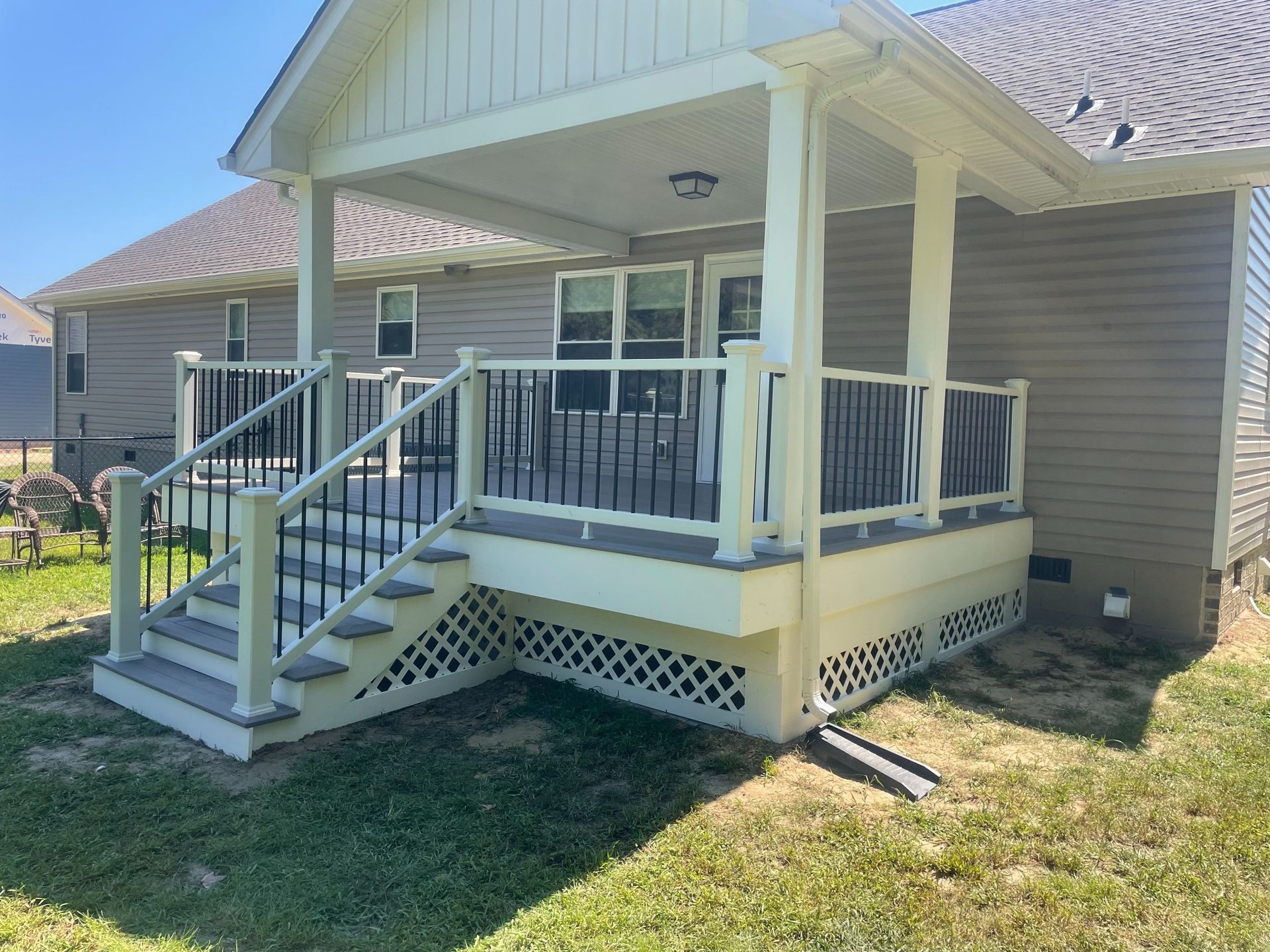 A light-colored covered deck with stairs, black railing, and a gray composite deck surface.