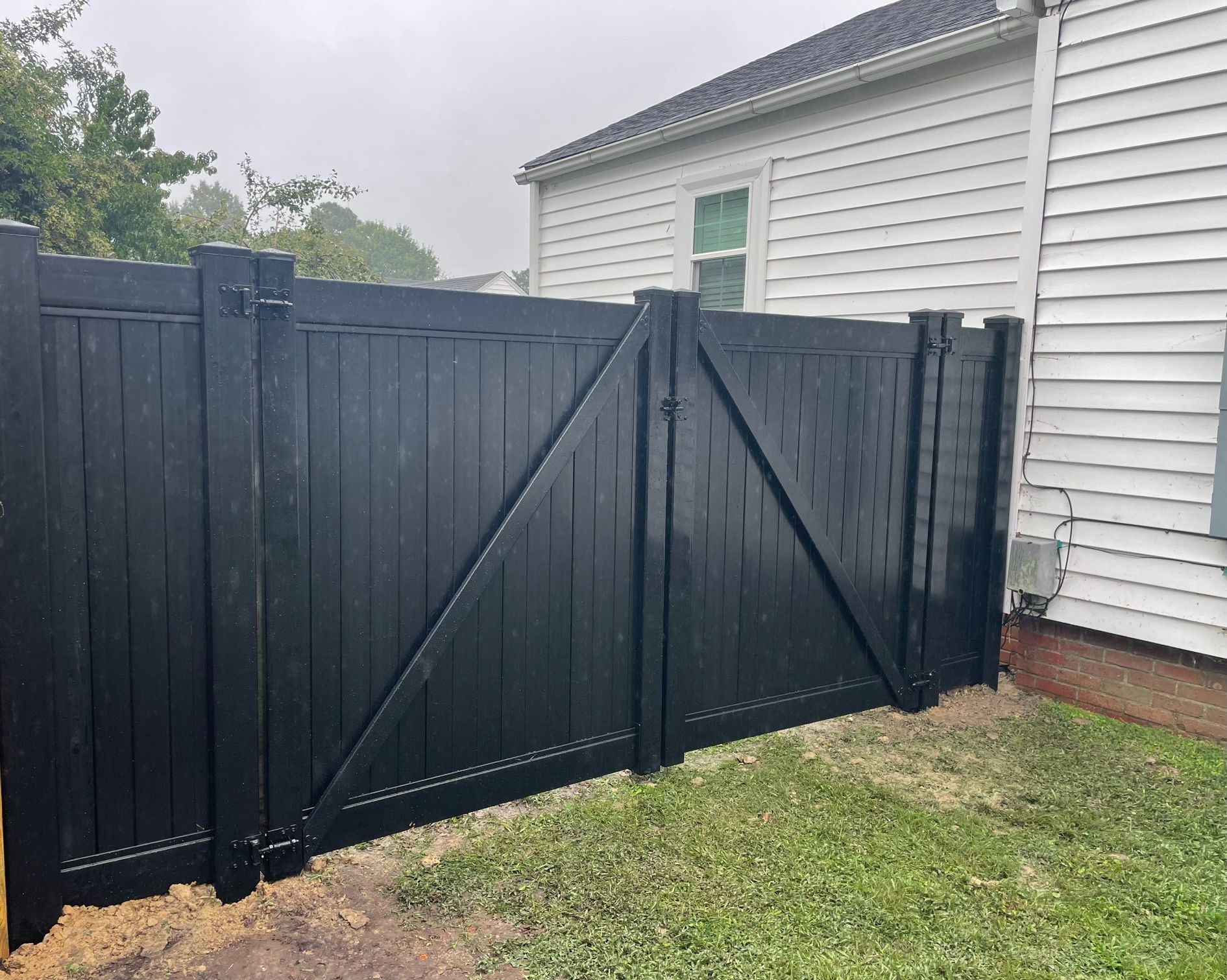 Black wooden fence with gate against a white house; green grass.