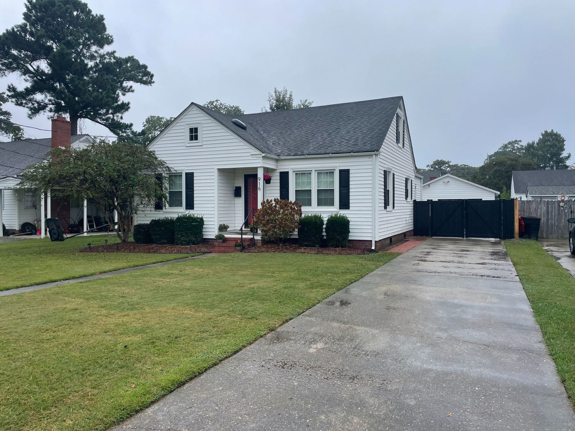 White house with black shutters, red door, and a long concrete driveway on a cloudy day.