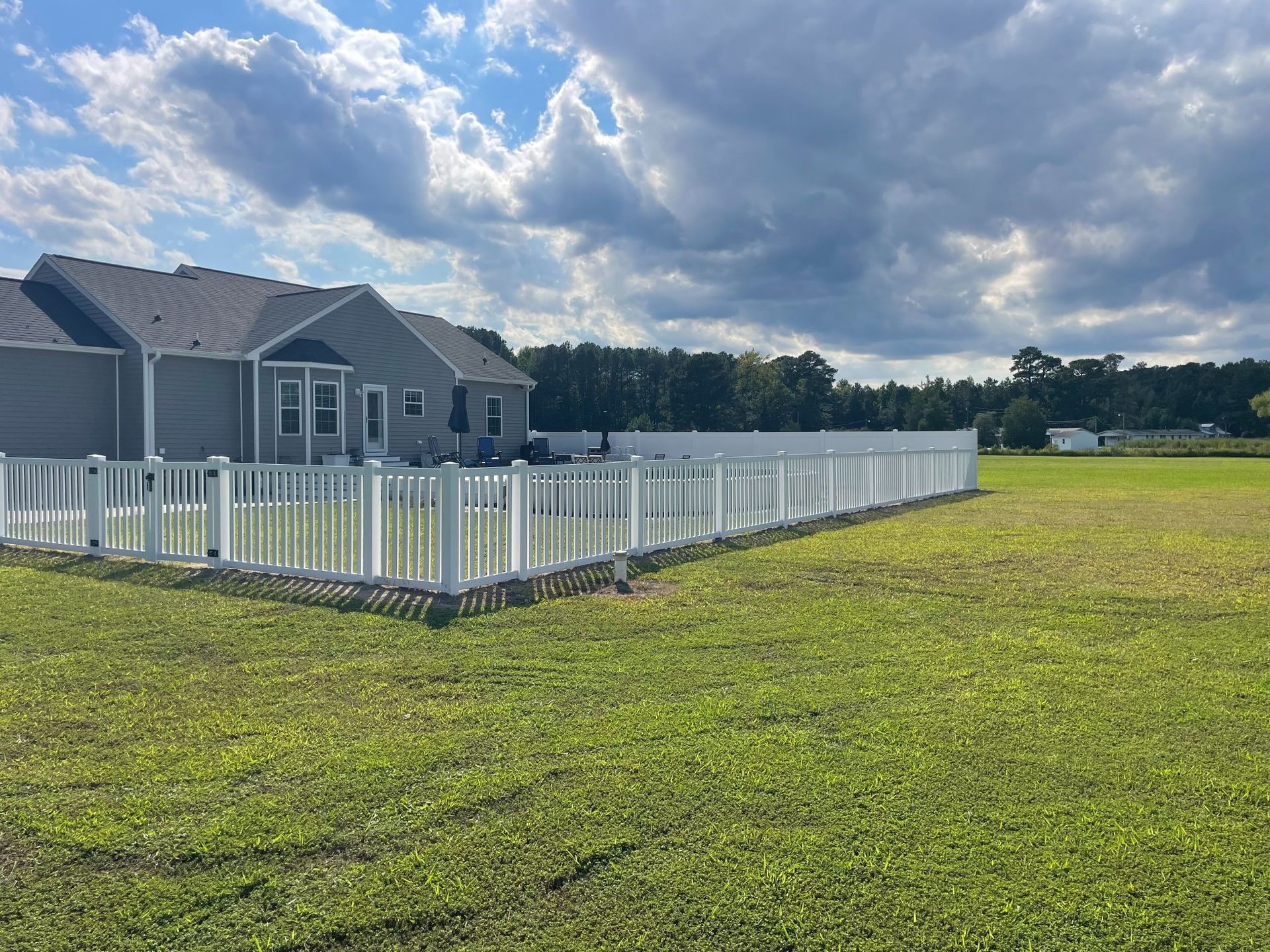 White picket fence around a house with green grass and a cloudy sky.