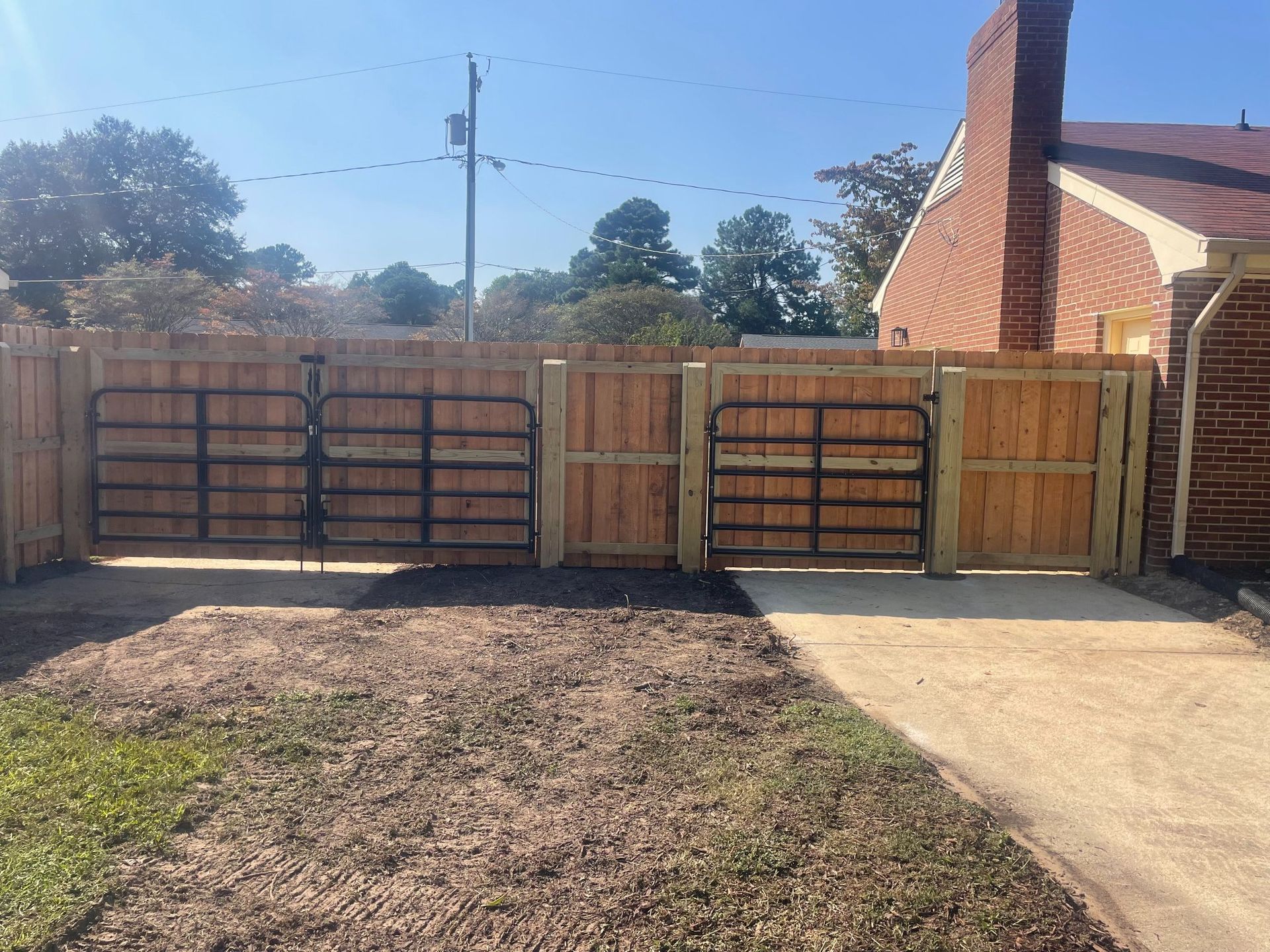 Wooden fence with black metal gates in front of a brick building.