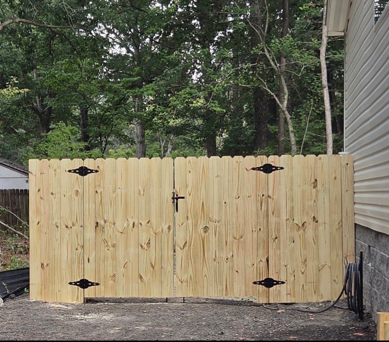 New wooden fence gate with black hinges and latch in a wooded backyard