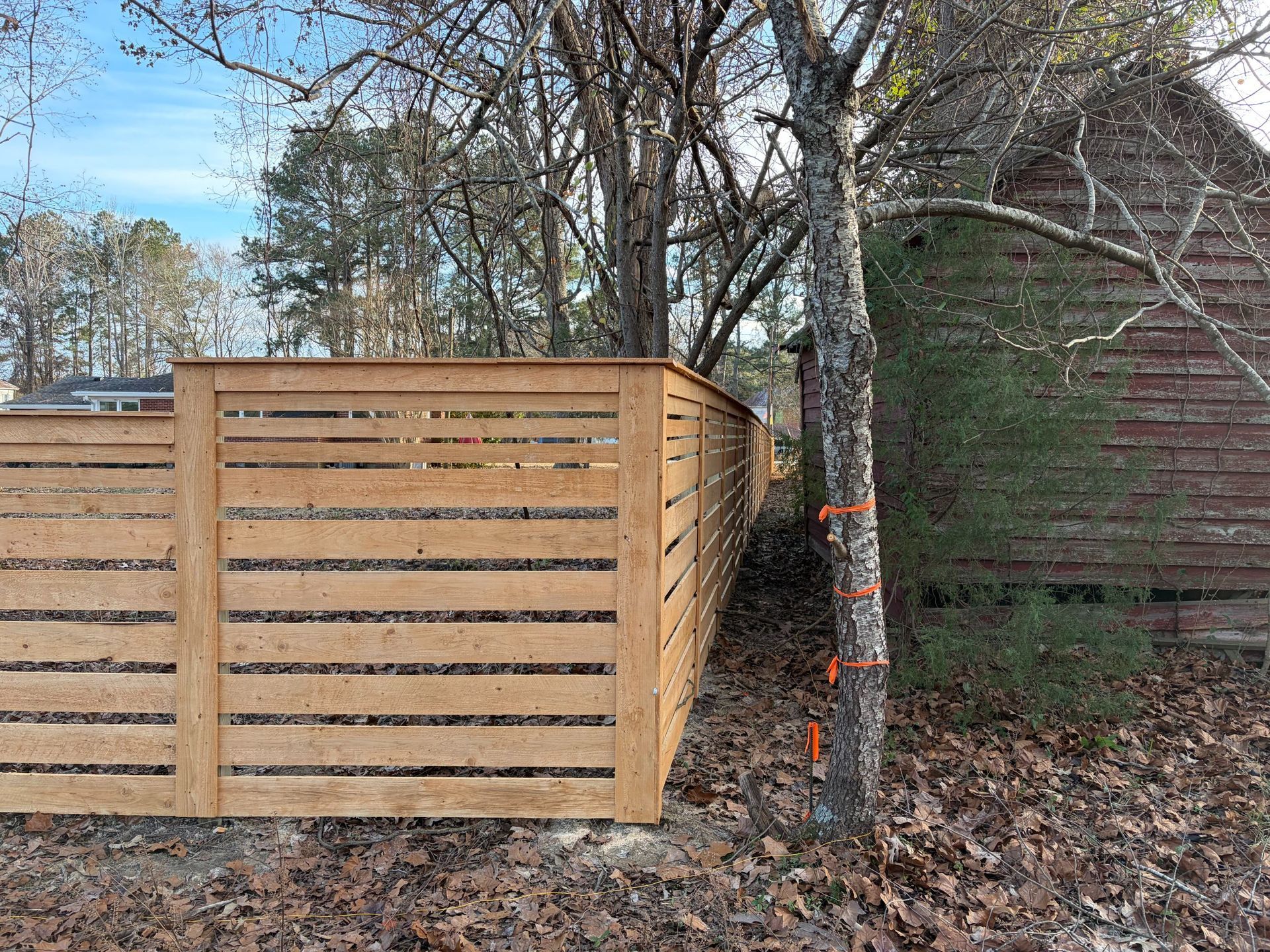 Wooden fence panels beside a tree in a leaf-covered yard