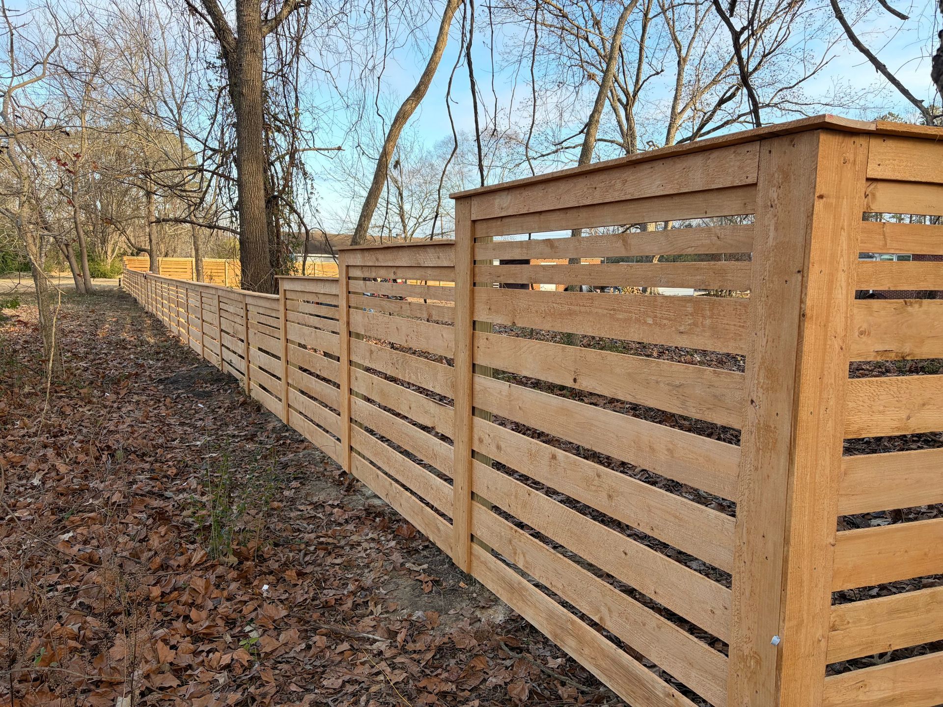 Long wooden slat fence along a leaf-covered path in a wooded area