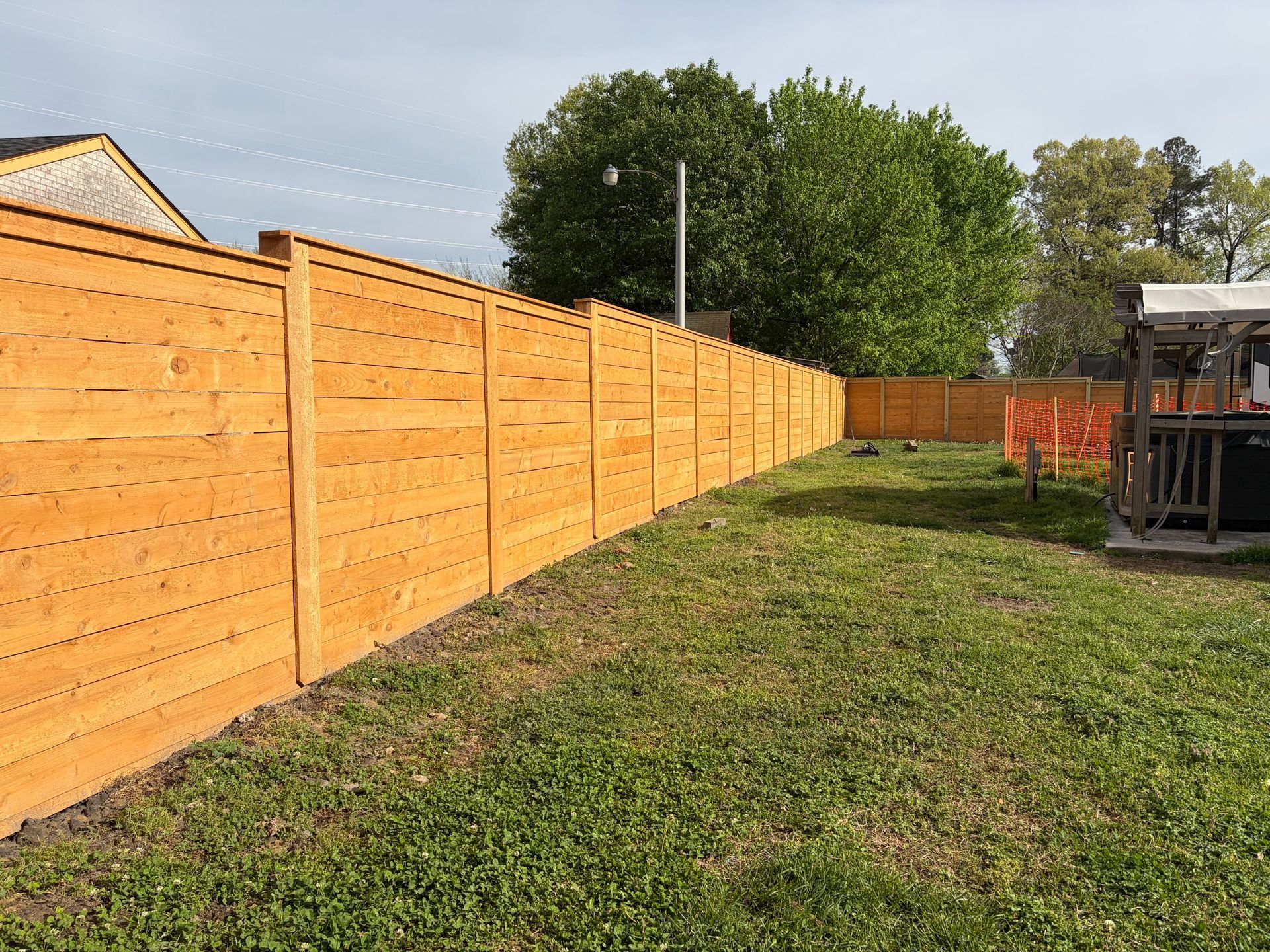 Backyard with a long wooden privacy fence, grass lawn, and a small patio structure on the right.