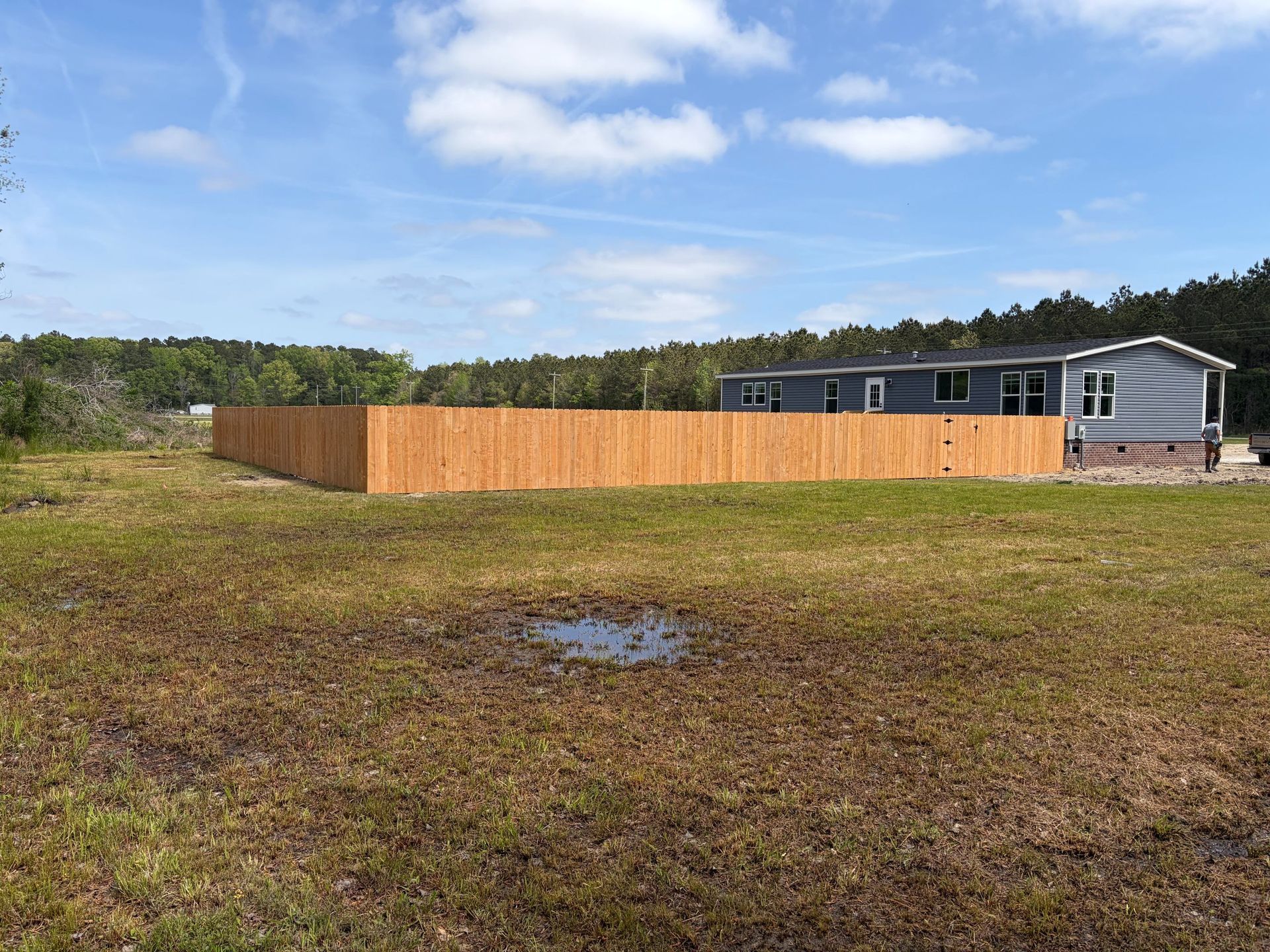 Grassy yard with a wooden fence and a gray house under a blue sky