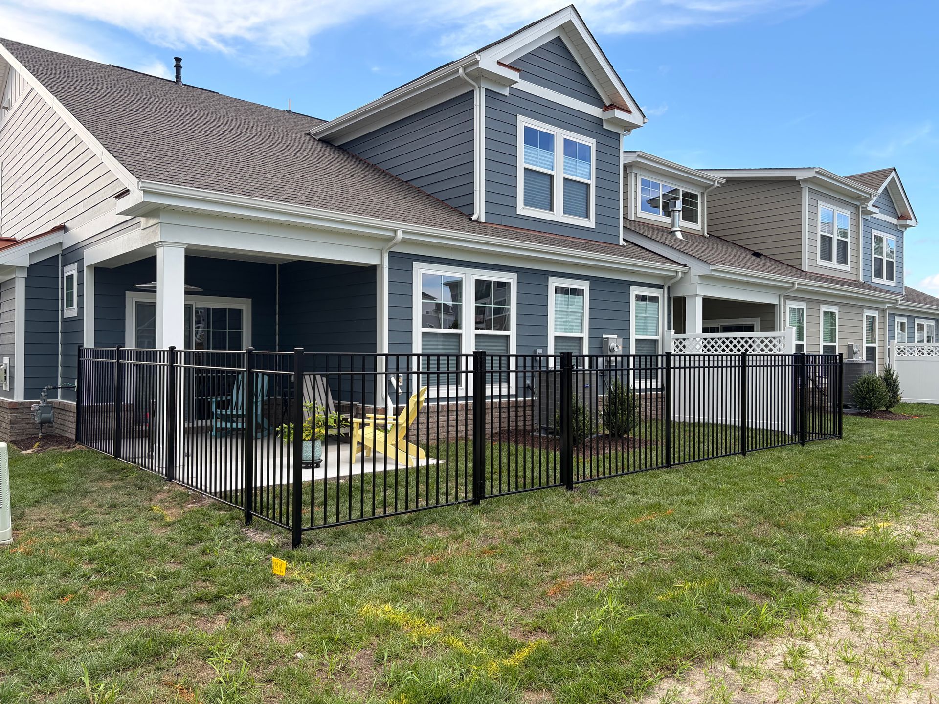 Row of blue-gray townhouses with black metal patio fences and a grassy shared yard under a cloudy sky