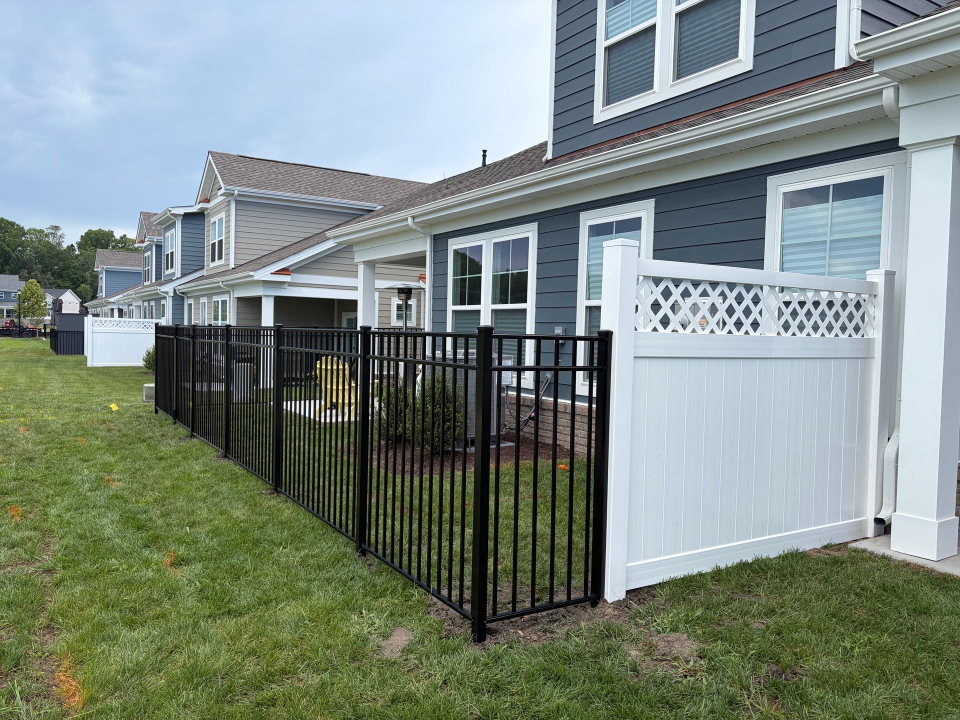 Row of townhouses with black metal and white vinyl fenced patios along a grassy walkway