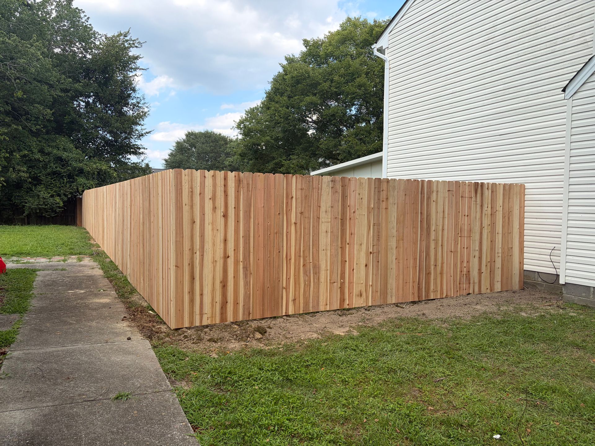 Wooden privacy fence enclosing a backyard beside a white house and sidewalk.