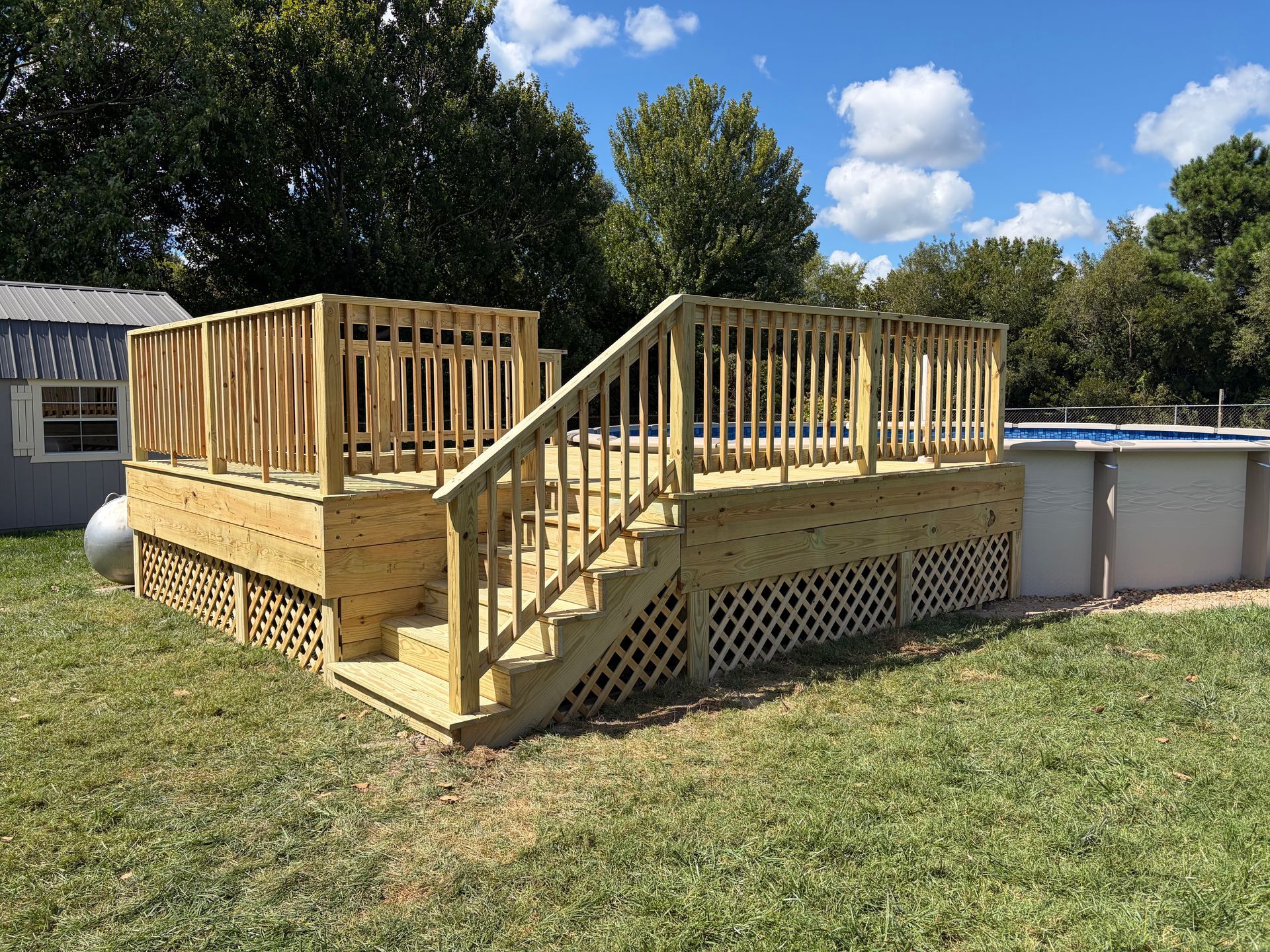Wooden deck under construction with stairs and railings beside a house and pool on a sunny lawn