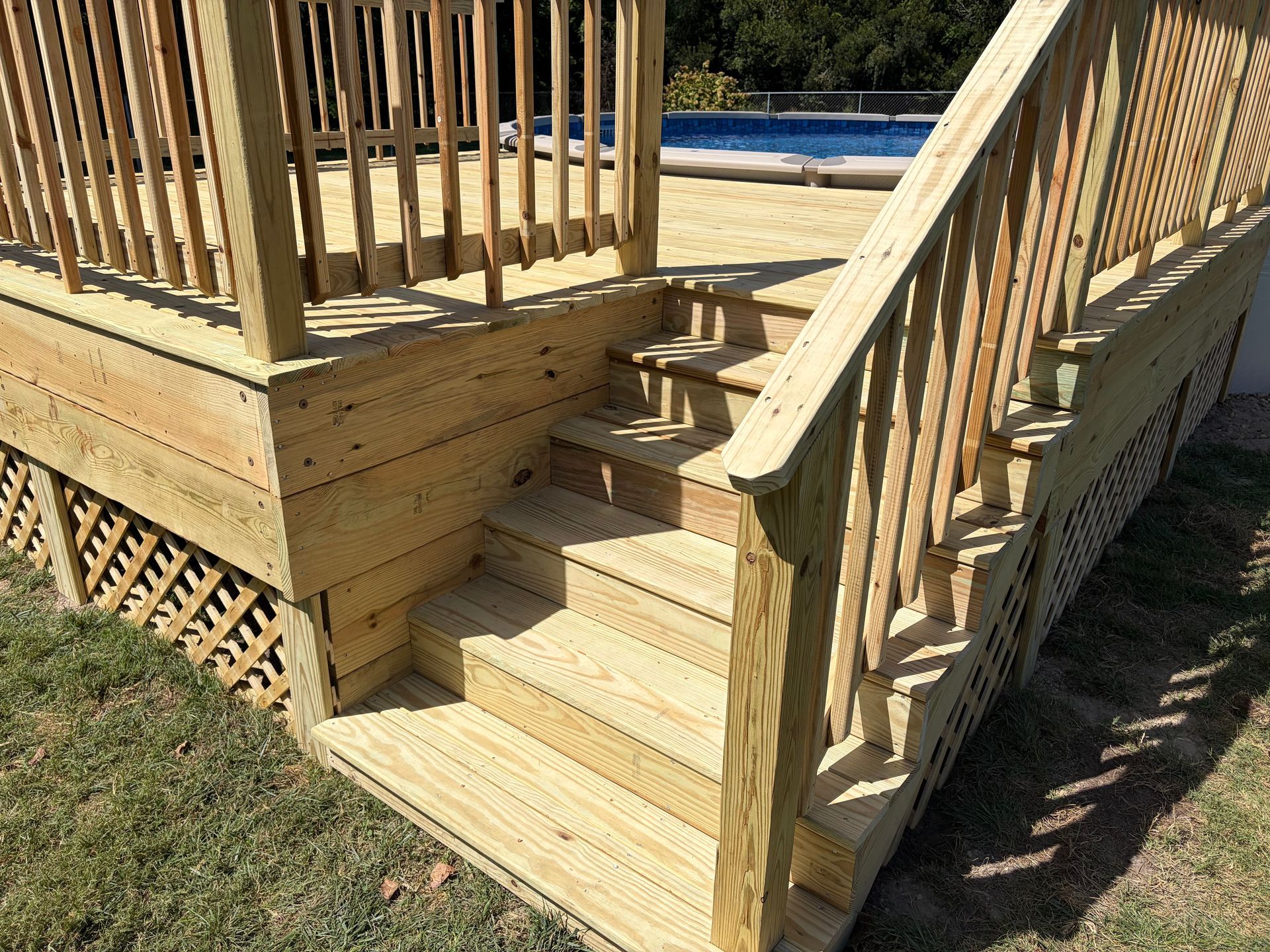 Wooden deck stairs with railings leading to an elevated porch in a sunny yard