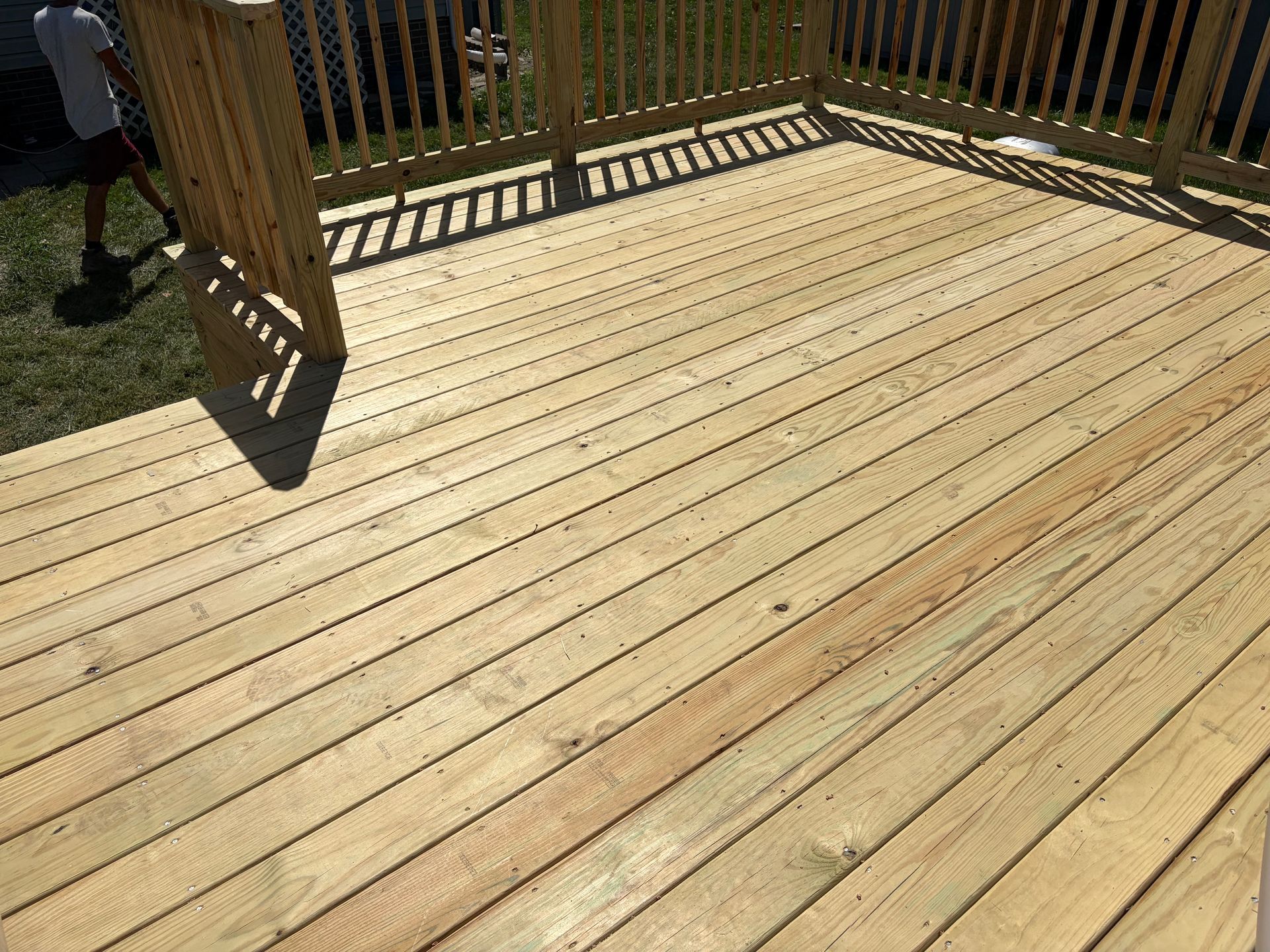 Sunlit wooden deck with railings and a shadow cast across the boards