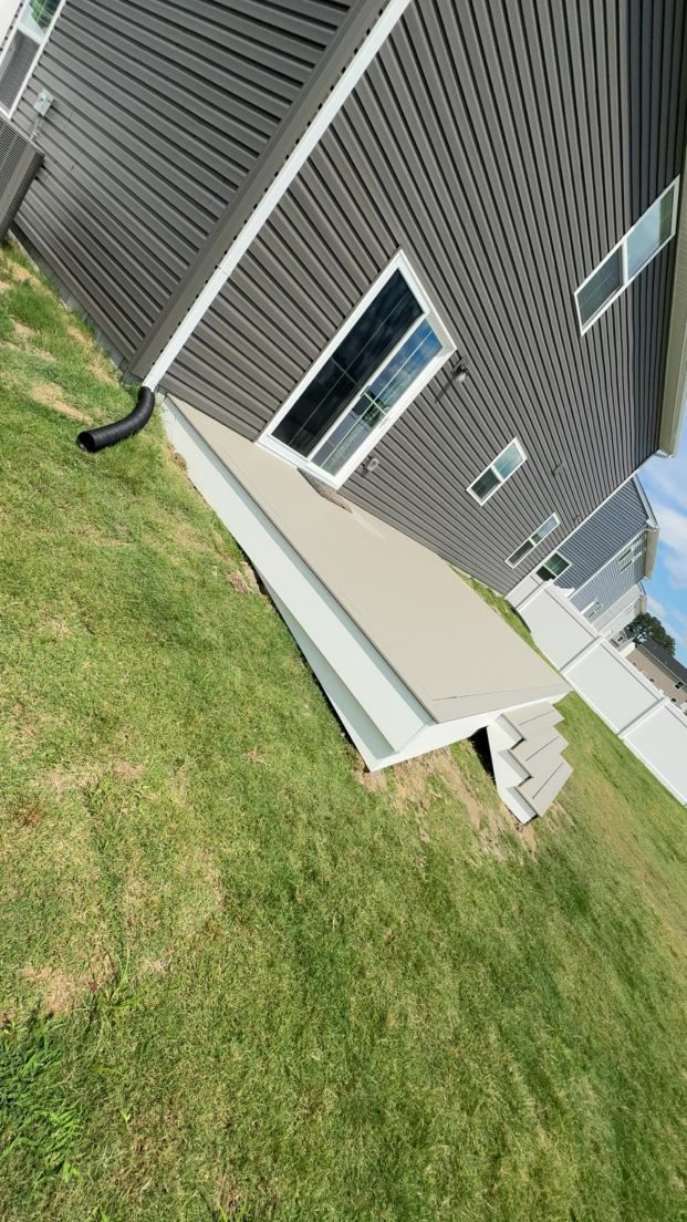 Tilted view of a house exterior with gray siding, white-framed windows, and a grassy lawn alongside a concrete path