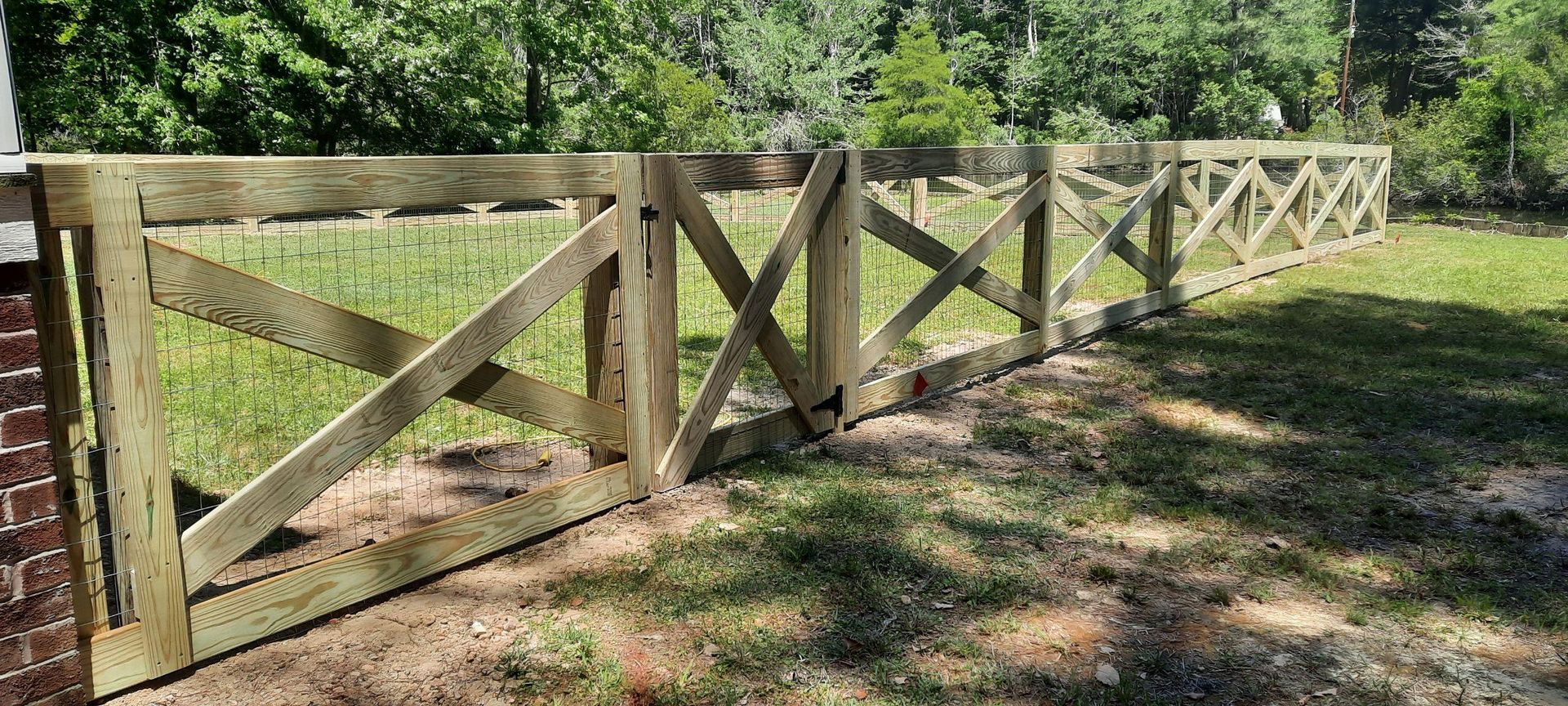 Wooden fence with X-braced panels along a grassy path in a sunny wooded area