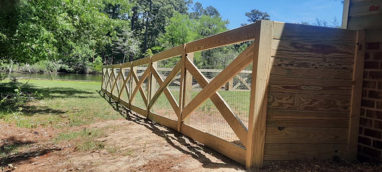 Wooden fence with X-braced panels along a dirt path beside a grassy wooded area