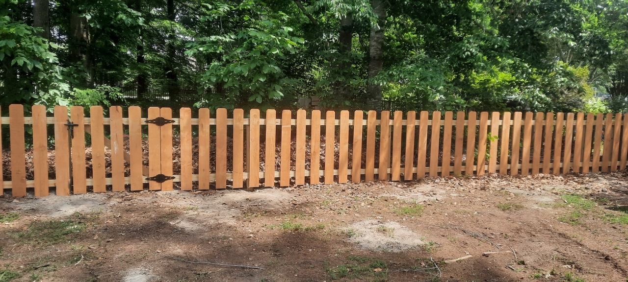 Wooden picket fence with green trees behind it along a dirt and gravel path