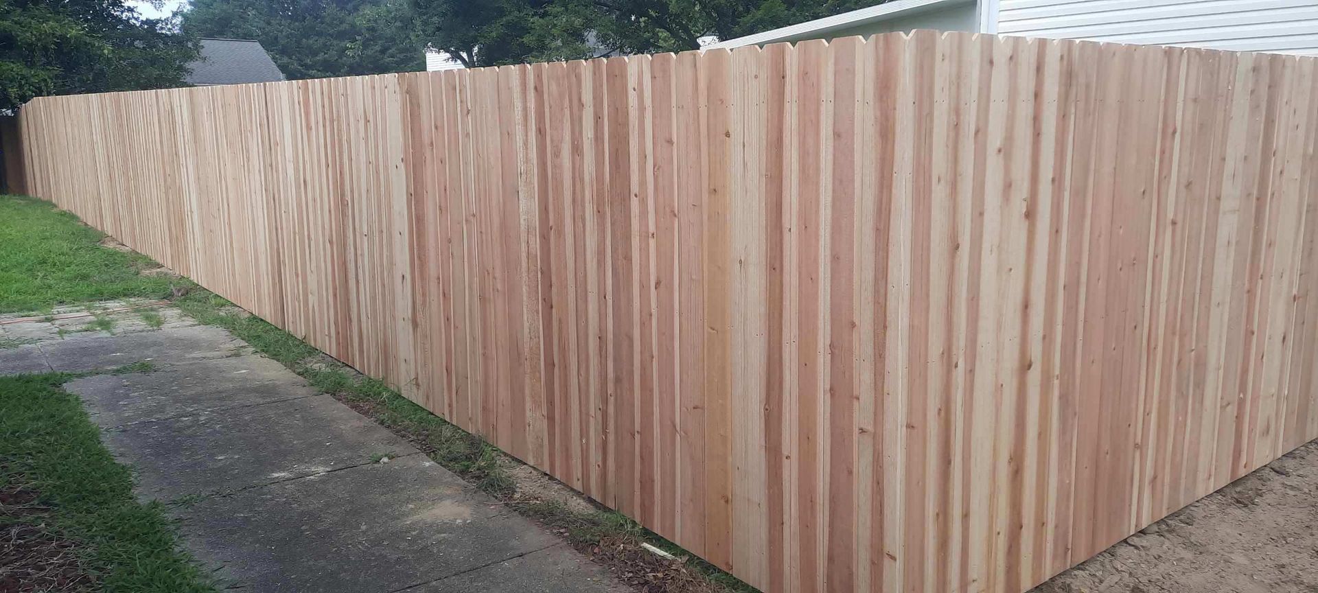 Wooden privacy fence along a sidewalk, with a small gate section at the corner.