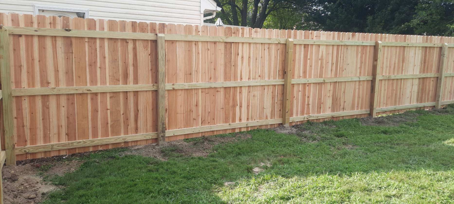 Wooden privacy fence bordering a grassy yard beside a brick house.