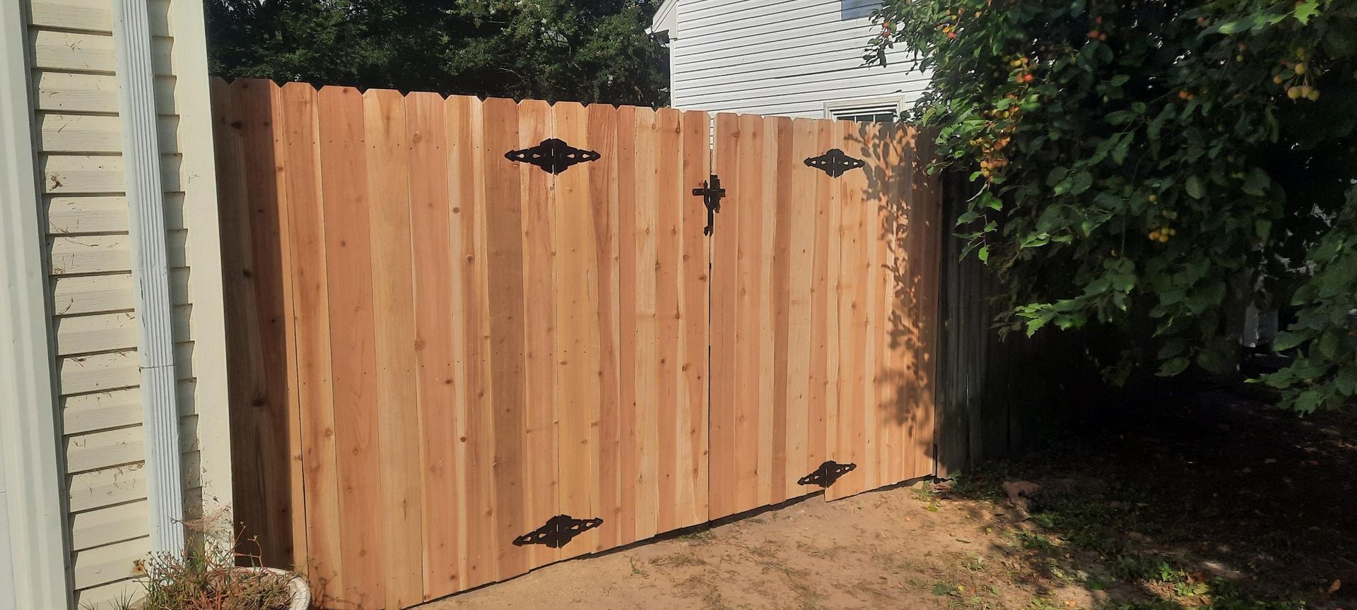 Wooden backyard gate with black hinges between a brick wall and dense greenery