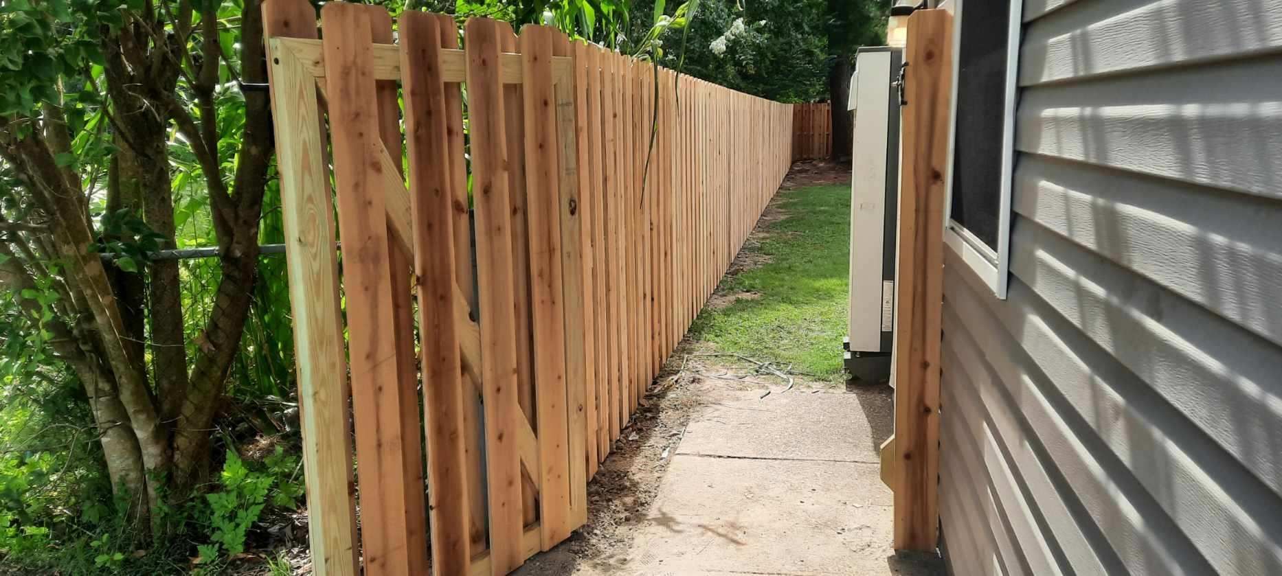 Narrow side yard with a wooden fence on the left and gray house siding on the right along a concrete path