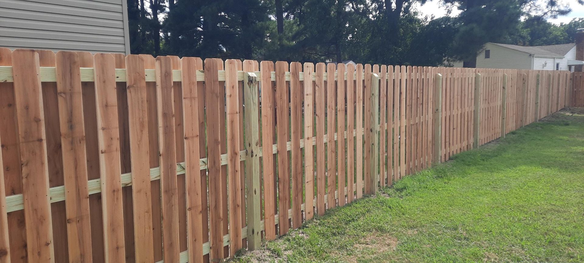 Long wooden privacy fence beside a grassy yard under a partly cloudy sky