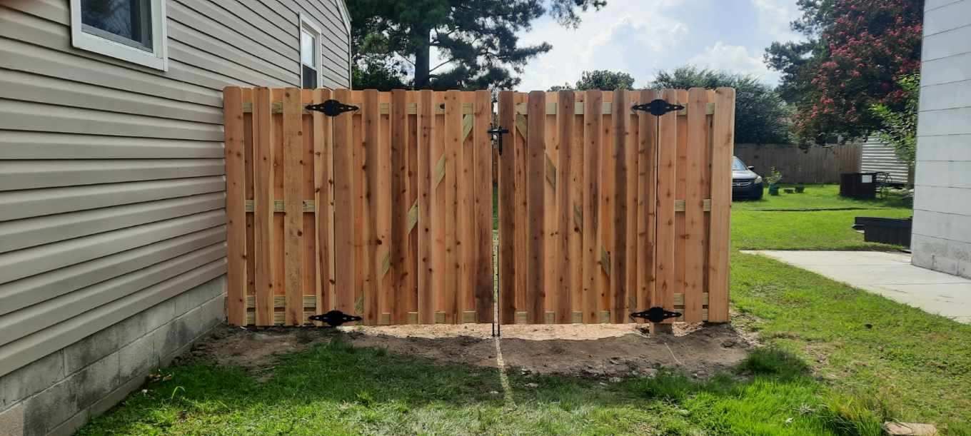 Wooden privacy fence beside a house, with a grassy yard and small garden bed