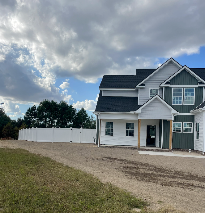 New two-story house with white siding and dark roof, gravel driveway, white fence, and cloudy sky.