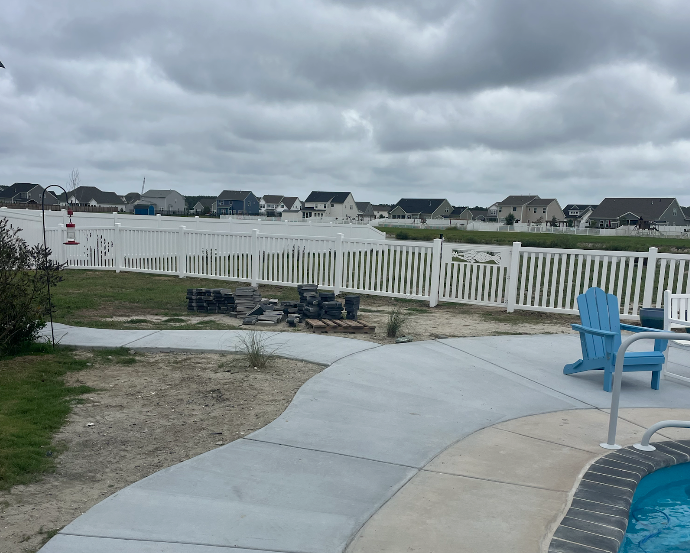 Backyard with white fence, pool, blue chair, overlooking water and houses on a cloudy day.