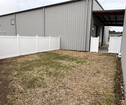 White fenced-in yard next to a gray building. Grass and gravel ground.