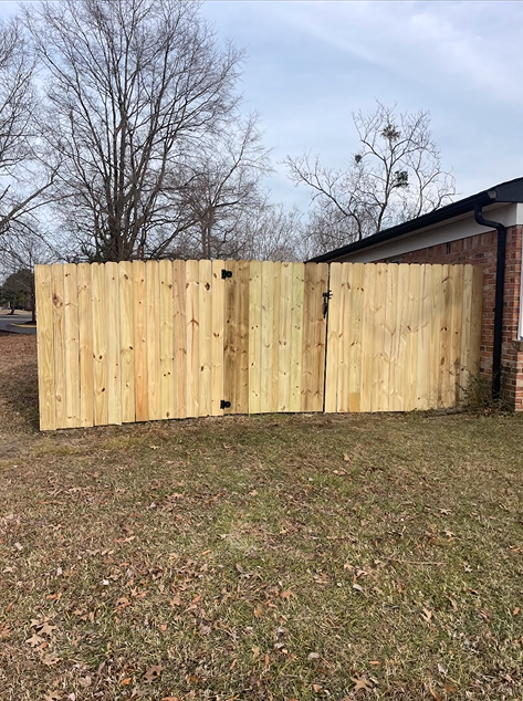 Wooden privacy fence with a gate next to a brick building and bare trees in the background.