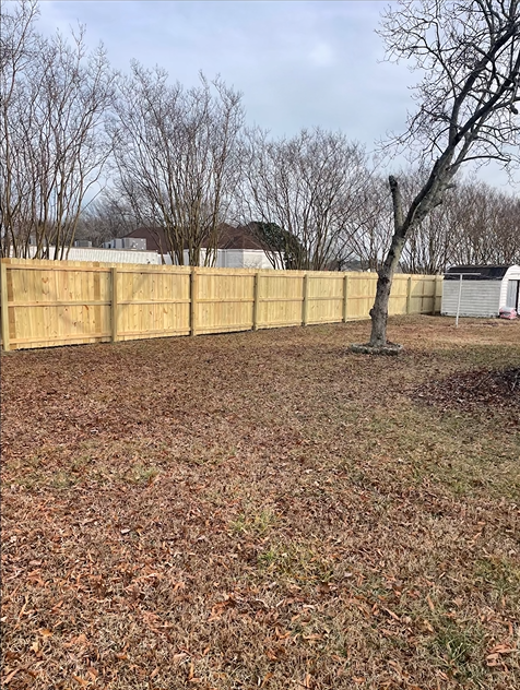 Wooden fence in a yard with brown leaves and bare trees on a cloudy day.