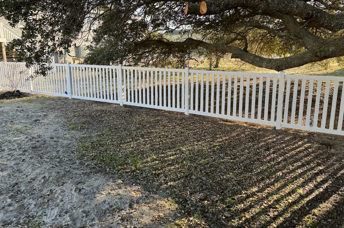 White picket fence under tree branches.