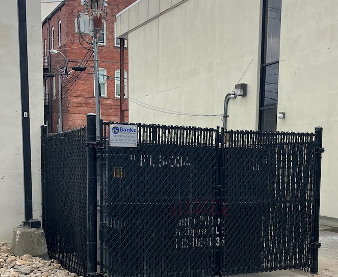 Black chain-link fence encloses an electrical utility area between two buildings.