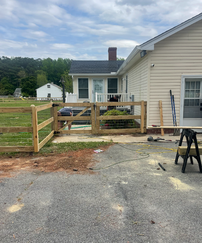 Wooden fence construction by a beige house on a cloudy day.